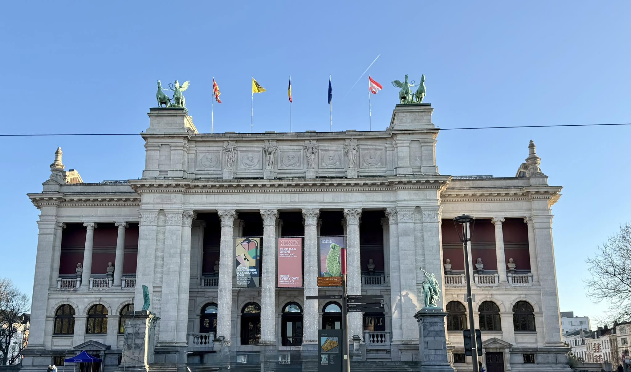 The neoclassical facade of the Royal Museum of Fine Arts Antwerp, its flags flying against a clear sky.