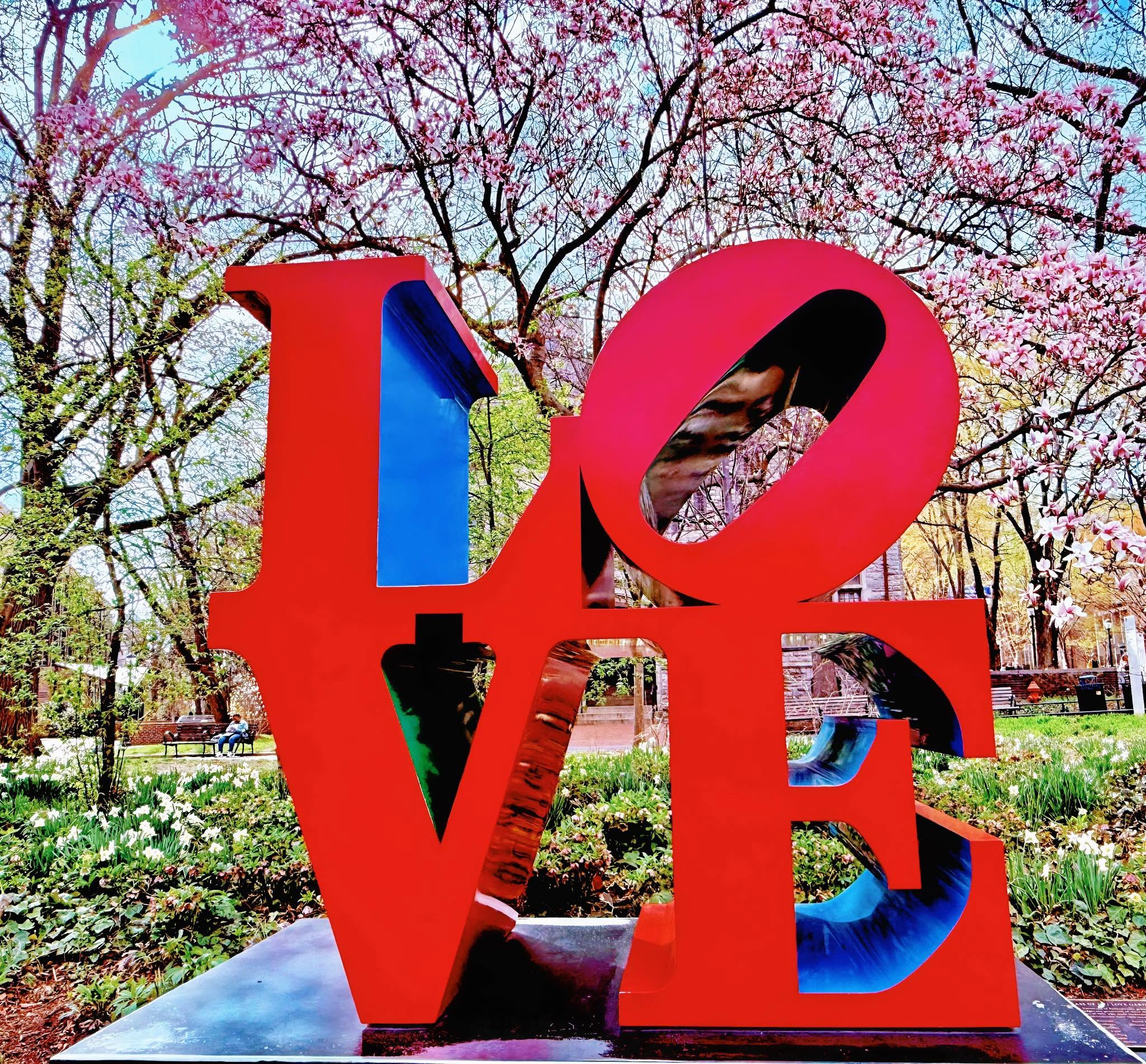 Robert Indiana's LOVE sculpture in a spring park, pink blossoms overhead.