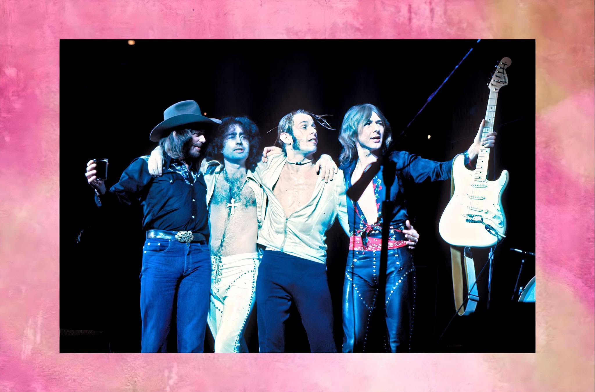 The four members of Bad Company onstage in the 1970s, arms around each other at the microphone.