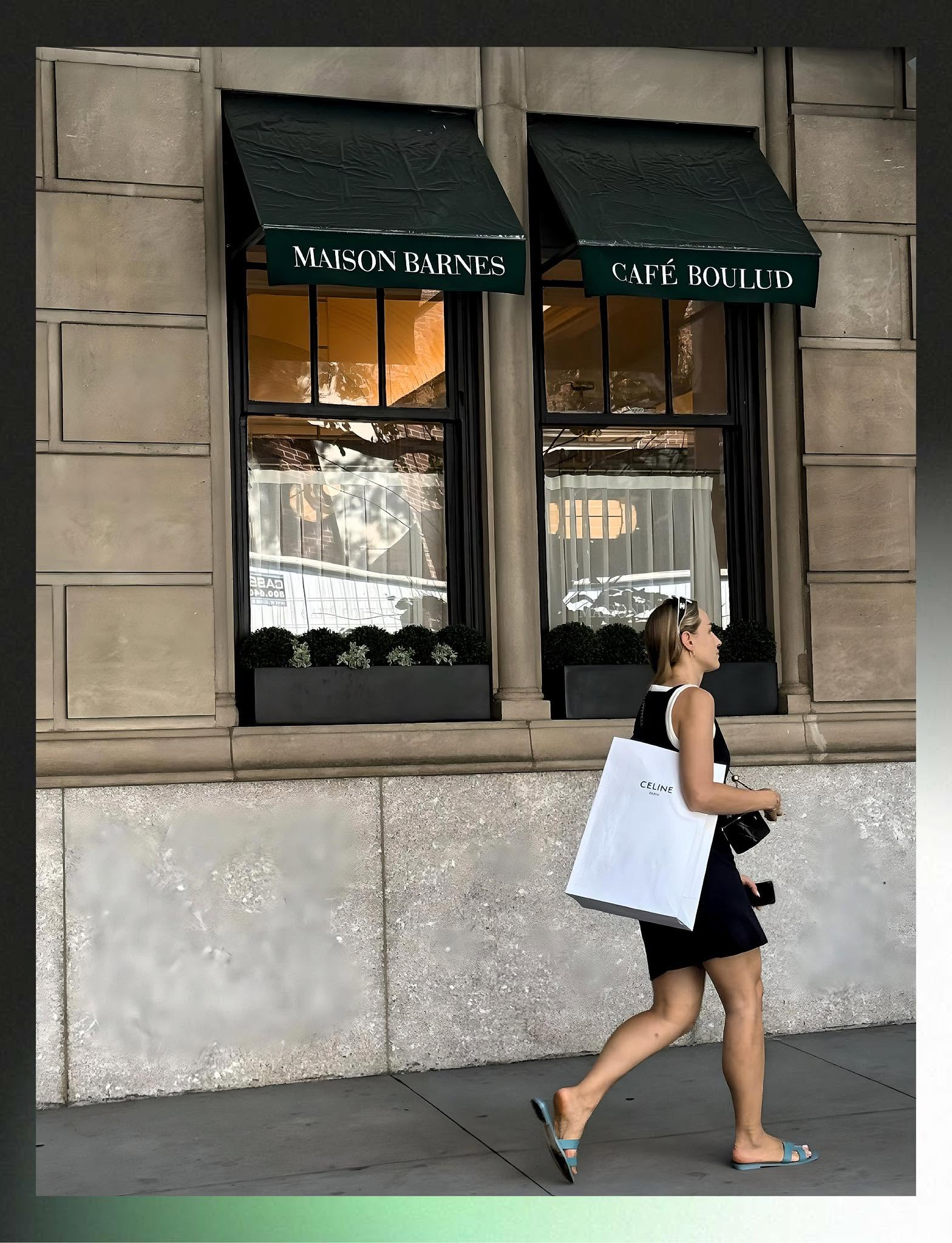 A shopper carrying a Celine bag walks past the green awnings of Café Boulud and Maison Barnes in Manhattan.