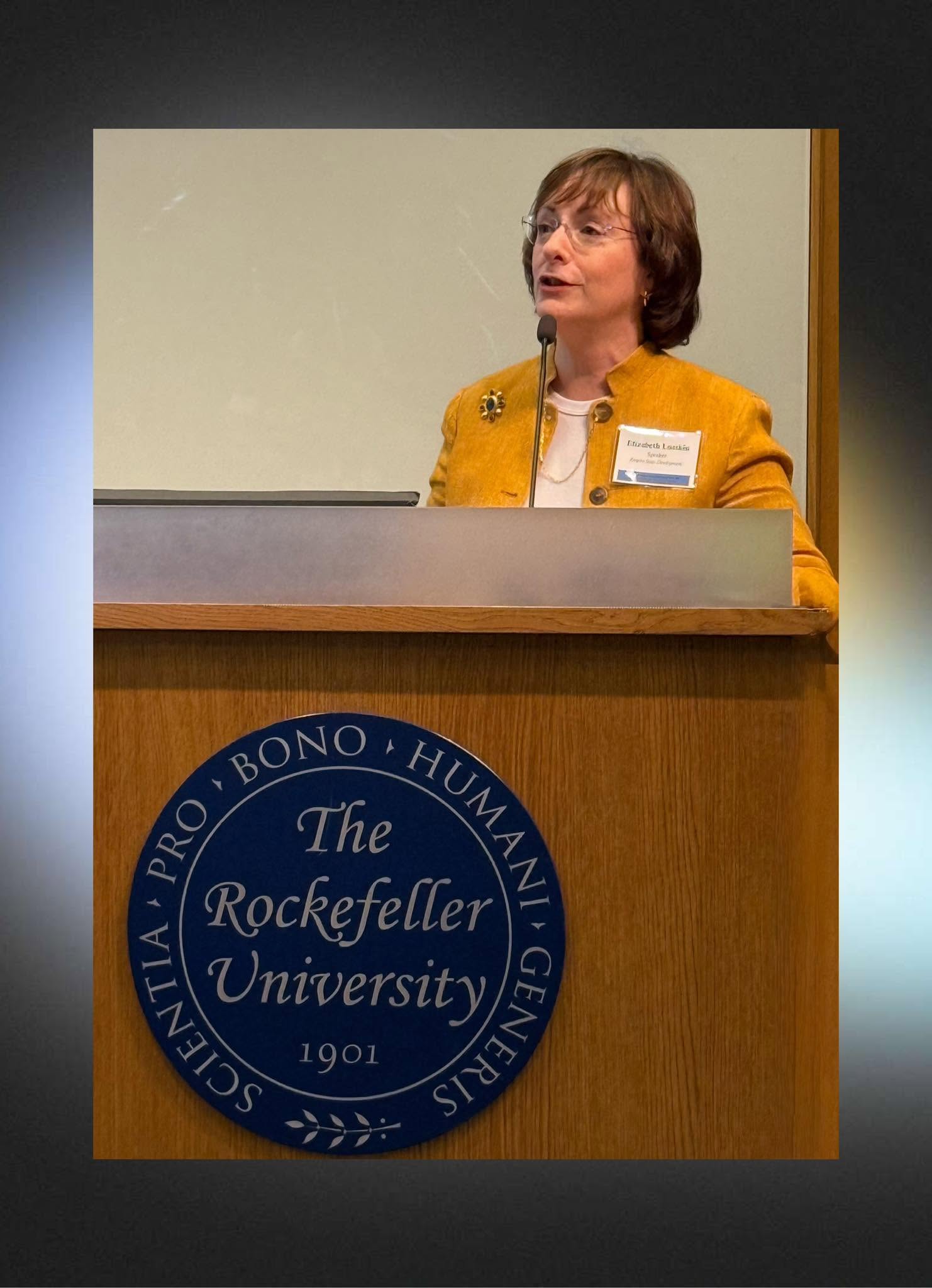 Elizabeth Lusskin speaks at a podium bearing the seal of Rockefeller University.