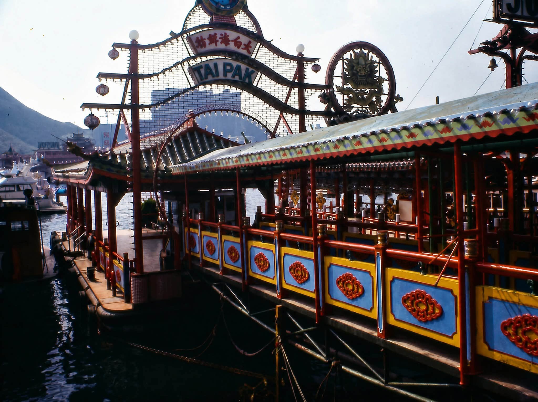 The Tai Pak floating restaurant pier in Aberdeen, Hong Kong, its red and yellow awnings bright against the harbor.