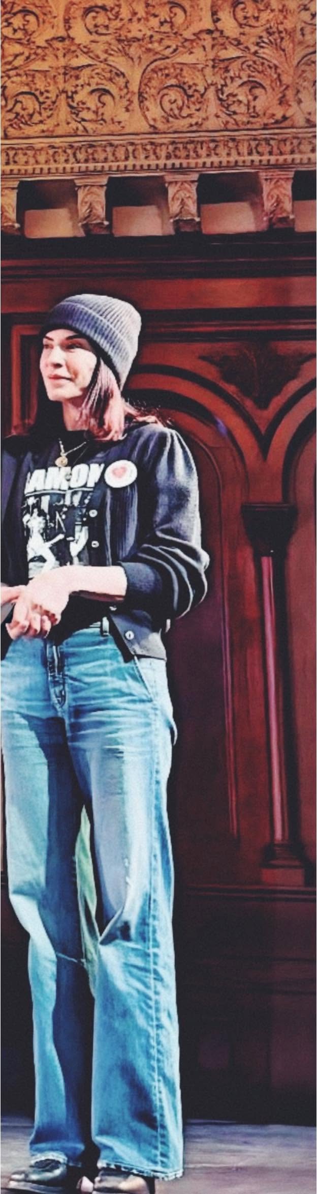 Julianna Margulies onstage in a knit beanie, graphic T-shirt, cardigan, and jeans.