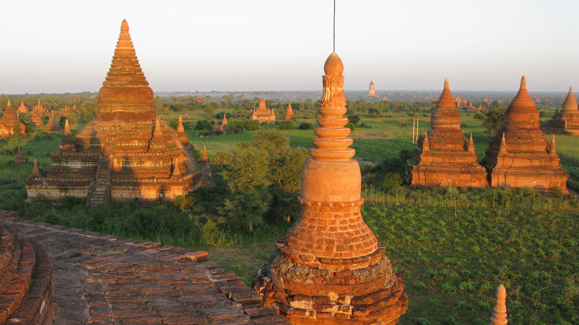 Brick stupas and temples of Bagan, Myanmar, glowing orange in late-afternoon light across a green plain