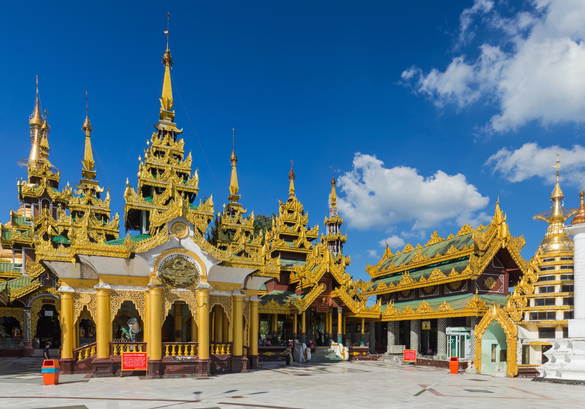 The gold-covered main stupa of the Shwedagon Pagoda in Yangon, ringed by smaller gilded shrines, with pilgrims on the marble platform
