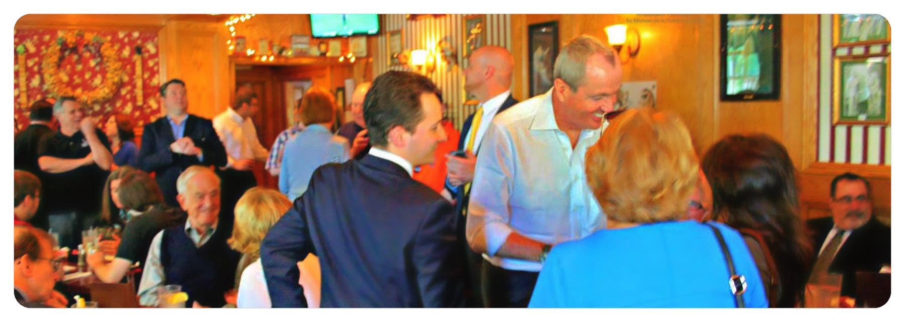 Gov. Phil Murphy mingles with a crowded room of guests in a wood-paneled restaurant.