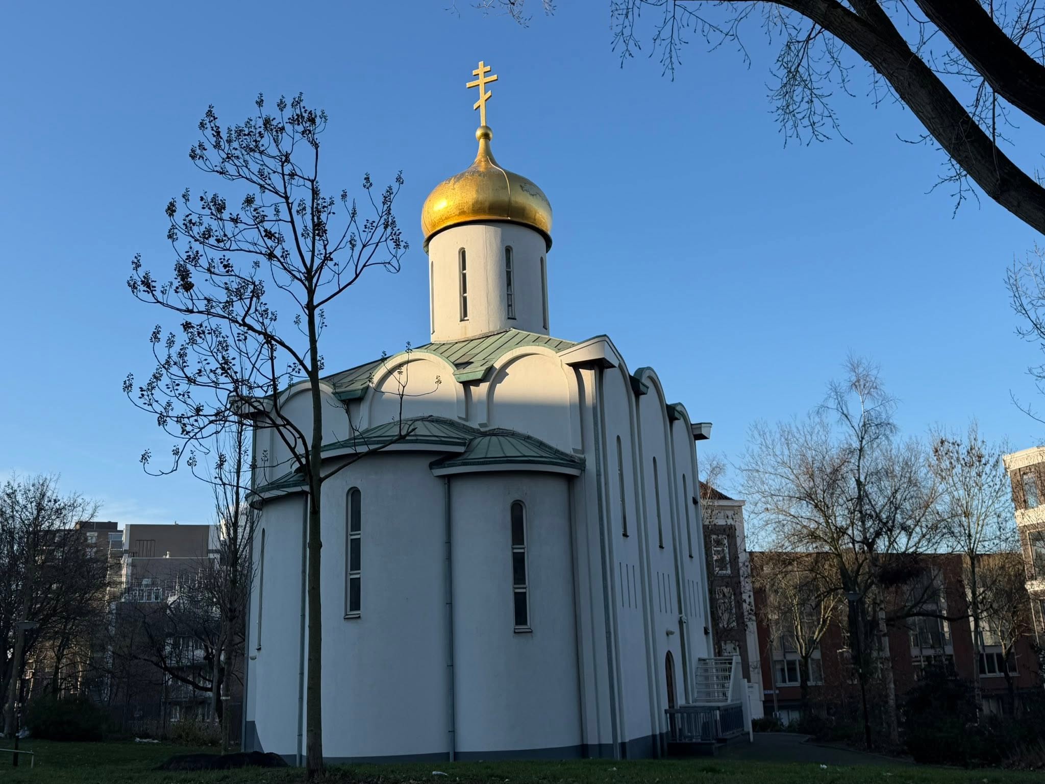 A white Orthodox church with a golden dome and cross rising against a clear blue sky in Rotterdam.