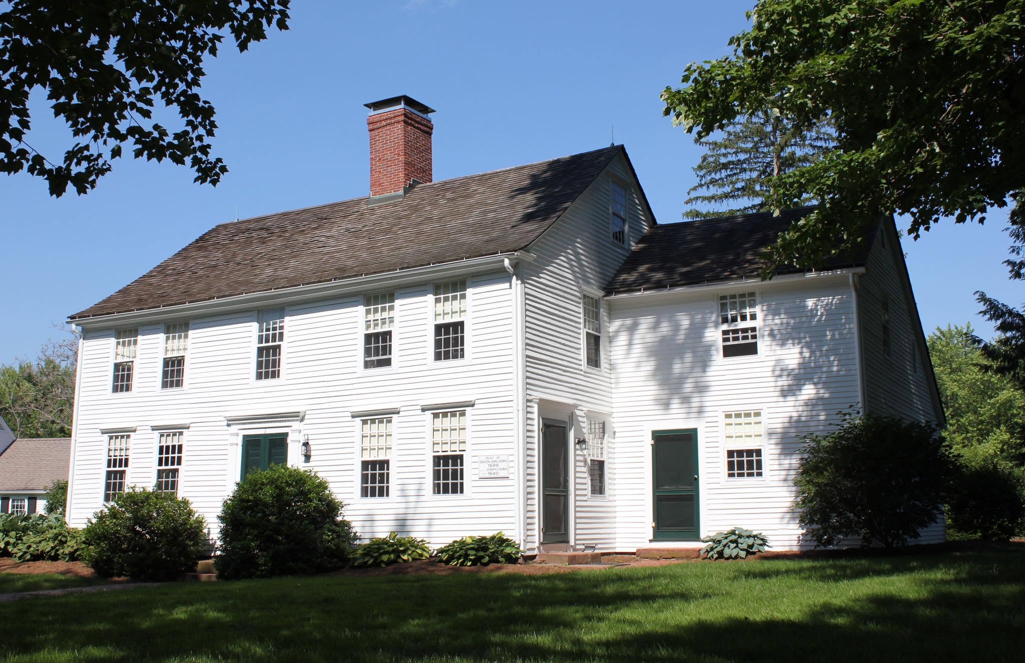 A white clapboard colonial-era house with green shutters under a clear blue sky.
