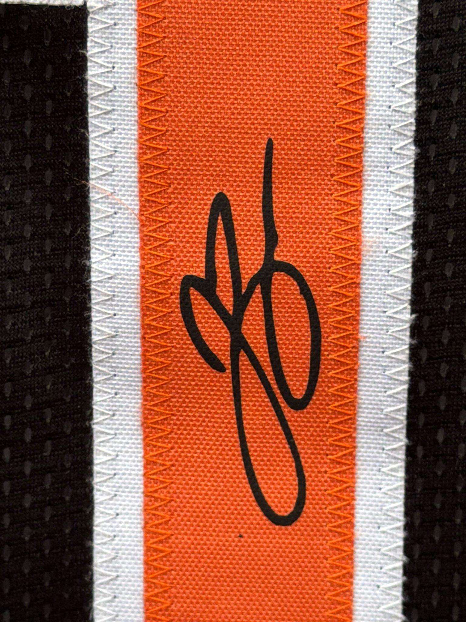 Close-up of a signature in black on the orange side stripe of a black Knicks-style jersey