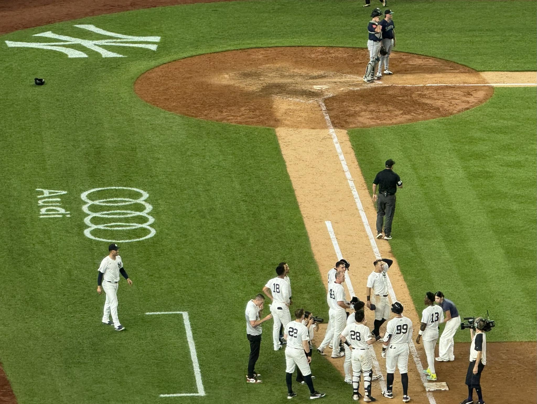 Yankees players gather near home plate on the infield while Mariners players stand by the mound