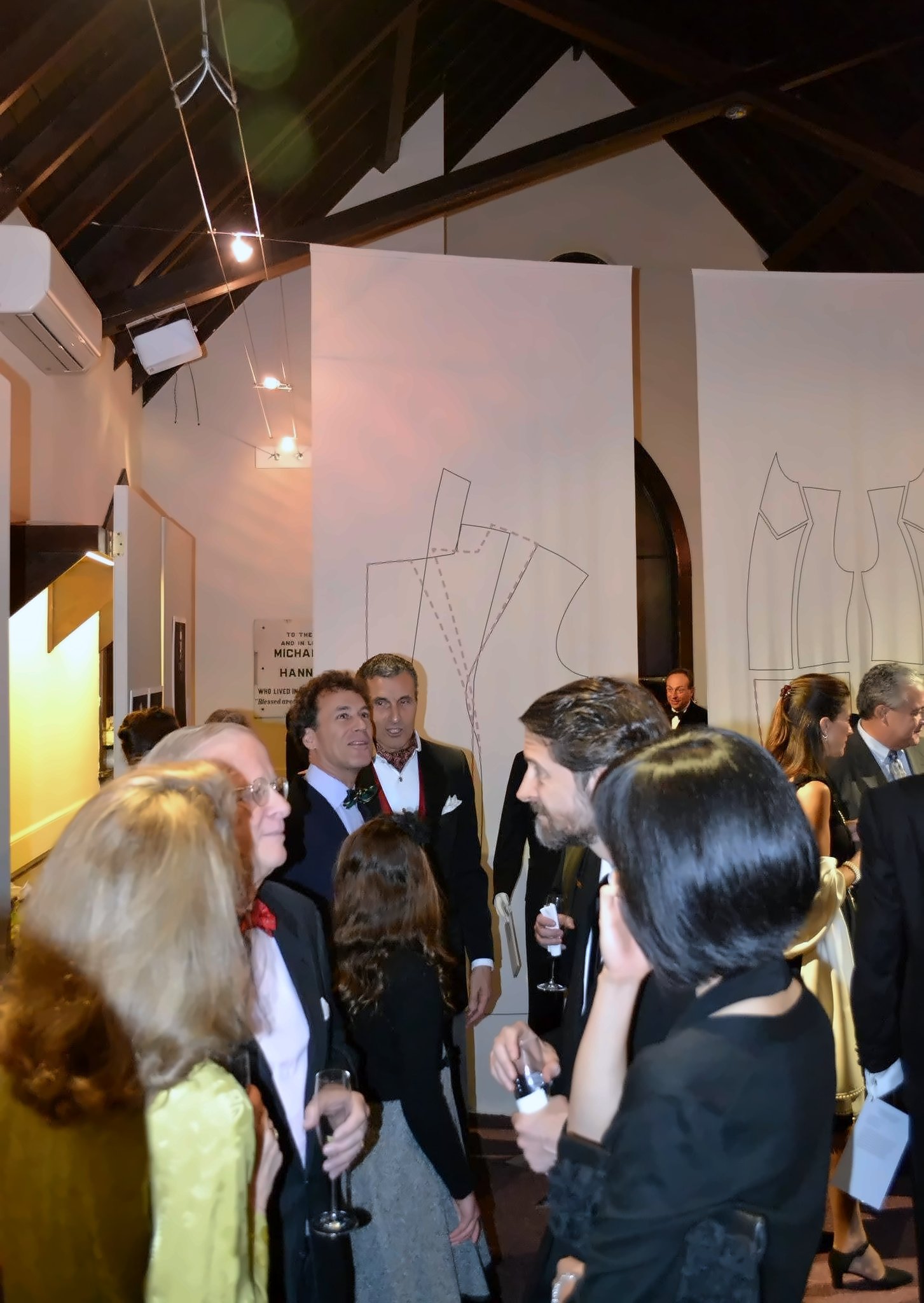 Under a dark timber roof, guests in bow ties and evening black move between the displays.
