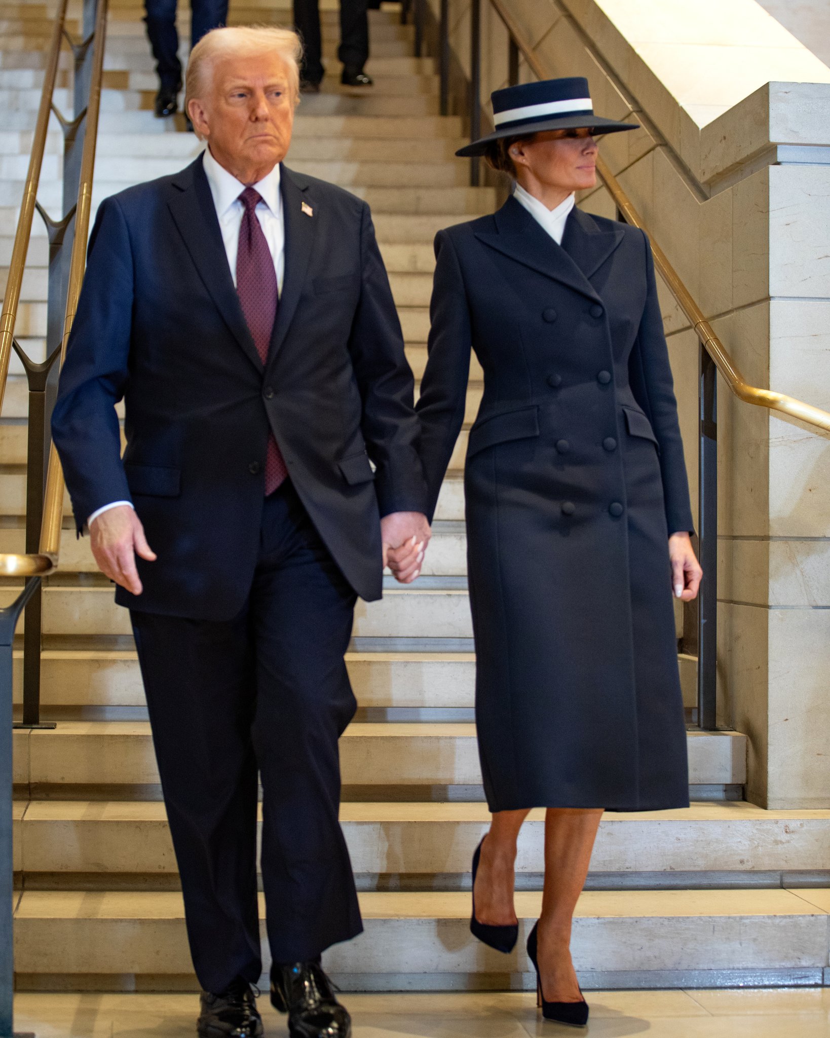 January 20, 2025: President Donald J. Trump and First Lady Melania Trump enter Emancipation Hall hand in hand; the First Lady wears Eric Javits's navy wide-brim hat and an Adam Lippes coat. Her other documented hat moments include a boater to visit Buckingham Palace in 2019, and at…