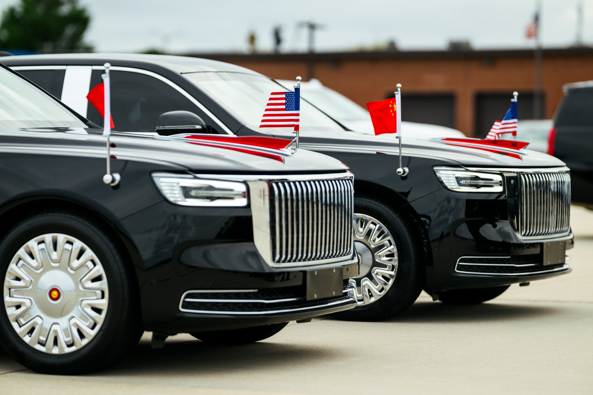 Joint Base Andrews, September 23, 2026: two black Hongqi state limousines, with vertical chrome grilles and spoked silver wheels, fly the flags of China and the United States from their fenders.