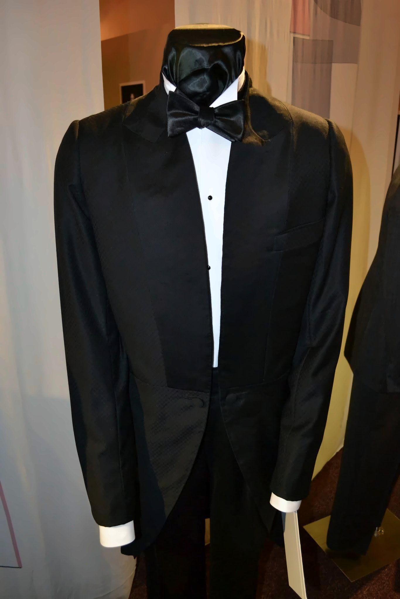 An evening coat on a mannequin, worn with a white shirt, white cuffs and a black bow tie.