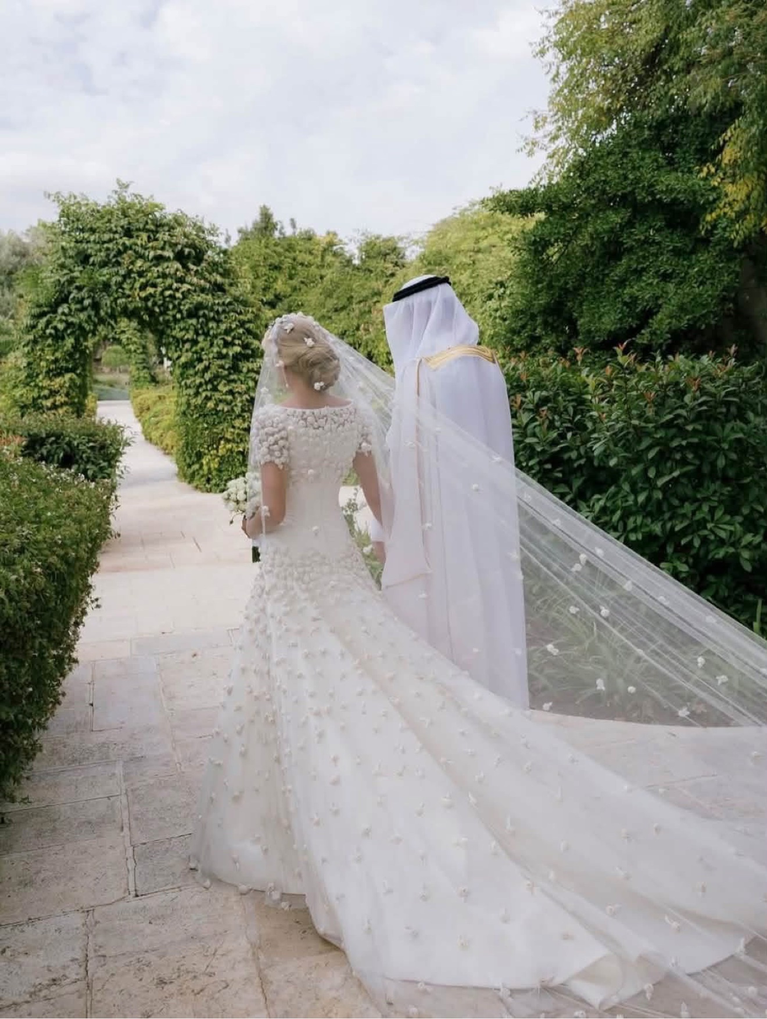 Princess Sara bint Faisal in the gardens of Zahran Palace, her embroidered veil and train spread behind her