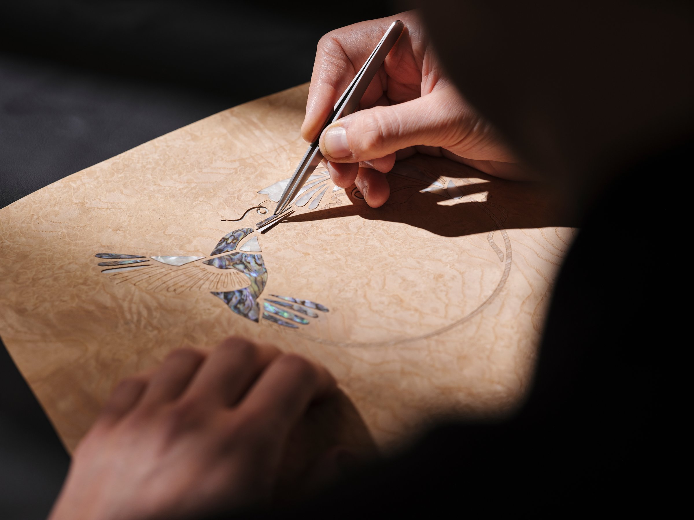 A Rolls-Royce craftsperson placing a fragment of shell into the hummingbird marquetry with tweezers